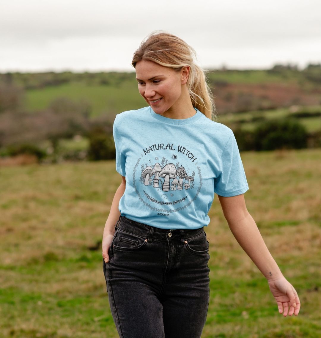 light blue organic t-shirt on a blonde haired model that says natural witch with mushrooms, moons and stars, designed by MooksGoo