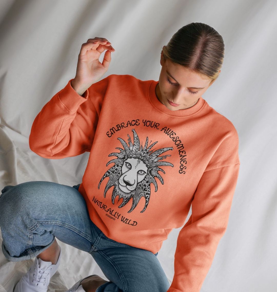 Model with brown hair wearing an Apricot organic cotton oversized sweatshirt with embrace your awesomeness naturally wild fun typography, and an illustrated wild lion, designed by MooksGoo