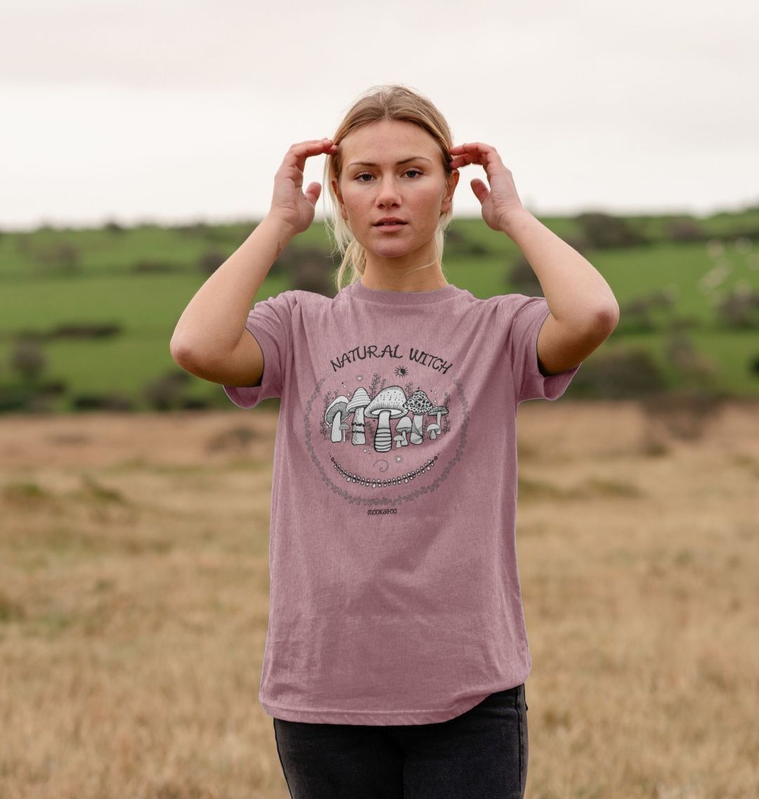sunset pink organic t-shirt on a blonde haired model that says natural witch with mushrooms, moons and stars, designed by MooksGoo