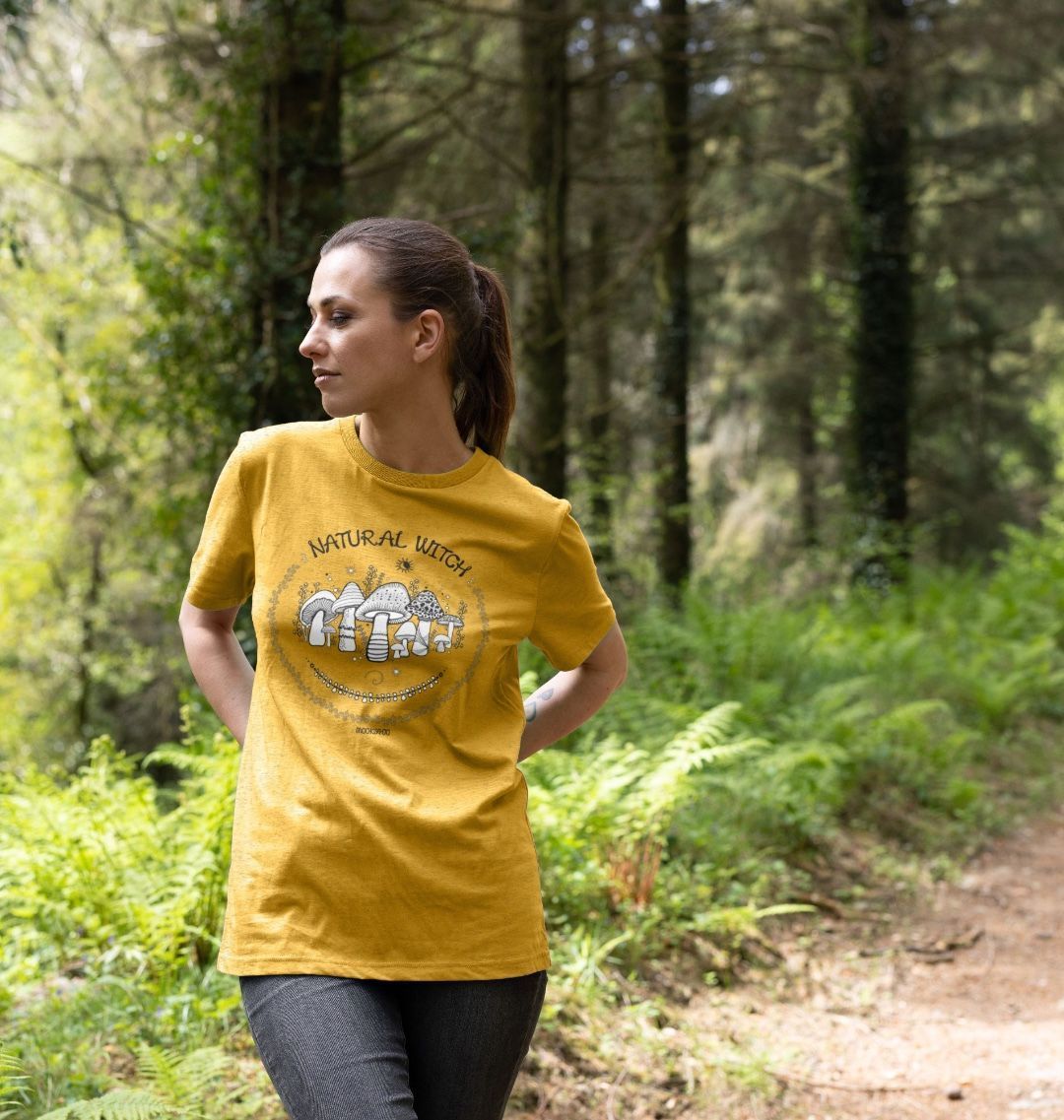 sunflower yellow organic t-shirt on a dark haired model in the woods, that says natural witch with mushrooms, moons and stars, designed by MooksGoo