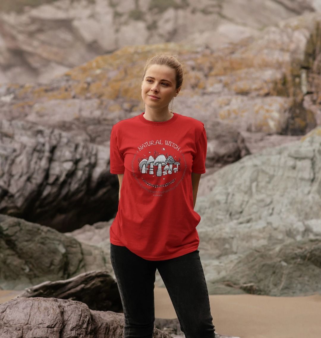 Blonde haired model outside on the Isle of Wight, wearing a red unisex t-shirt with white illustrations of mushrooms, toadstools, moons, stars, leaves and vines, with the words Natural Witch in funky typography, halloween spooky design by MooksGoo