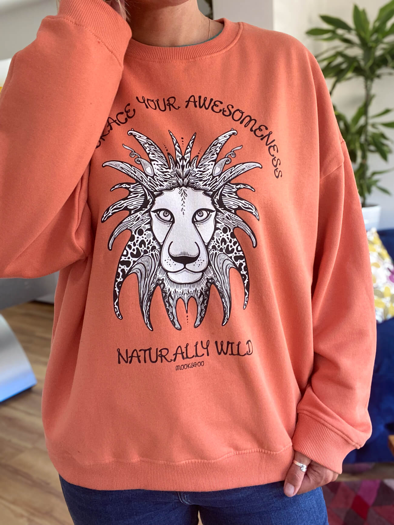 Model standing up wearing an Apricot organic sweatshirt with embrace your awesomeness naturally wild fun typography, and an illustrated wild lion, designed by MooksGoo