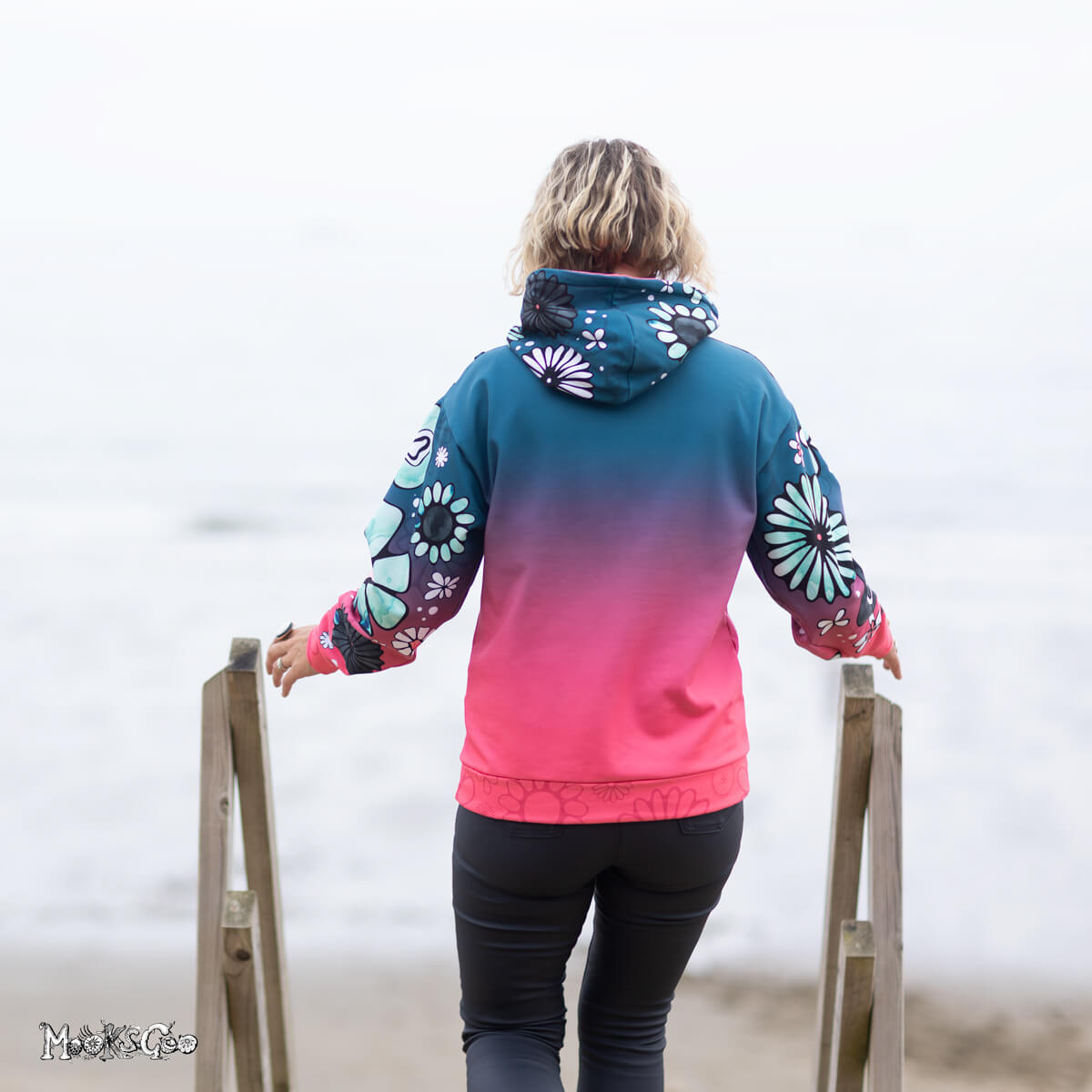 The back of the Colour Fade Flower Power Recycled Unisex Hoodie, modelled by Michelle Lott (MooksGoo) wearing a Size S. Photography by Julian Winslow at Shanklin beach front on the Isle of Wight