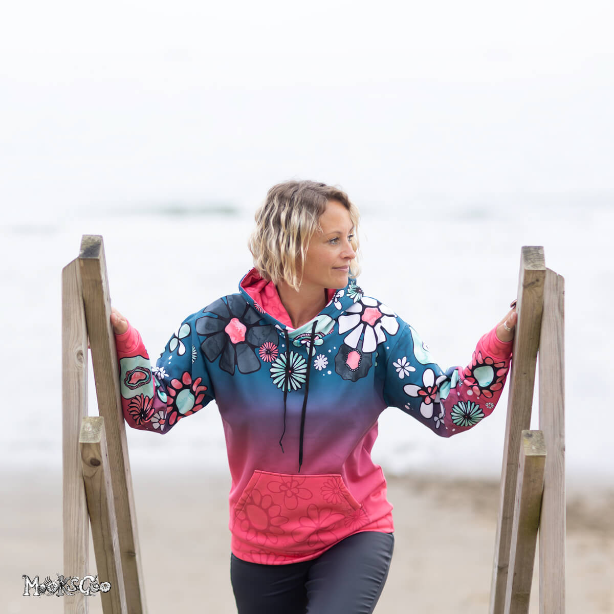 Michelle Lott (MooksGoo) modelling the Size Small Colour Fade Flower Power Recycled Unisex Hoodie, with watercolour illustrated flowers and bold teal with coral pink. Photography by Julian Winslow along Shanklin Esplanade on the Isle of Wight