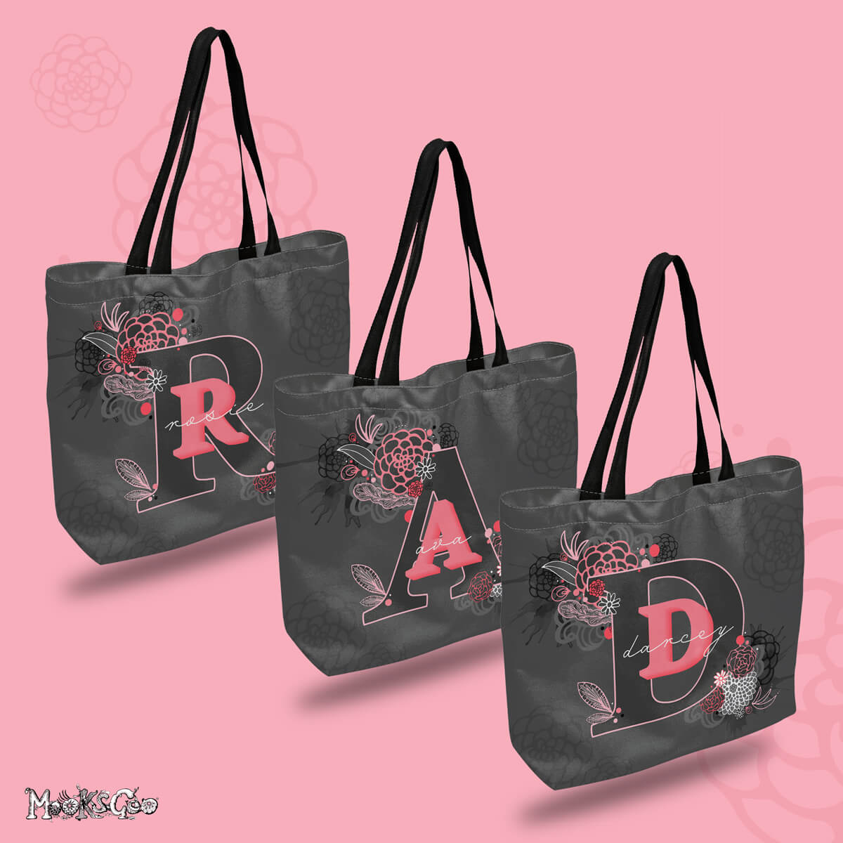 Personalised canvas tote bag, with a dark grey background, an initial in a bold font in a darker grey colour with pink outline, and a name in white with script writing. Illustrations are of flowers, feathers and watercolour splashes designed by MooksGoo