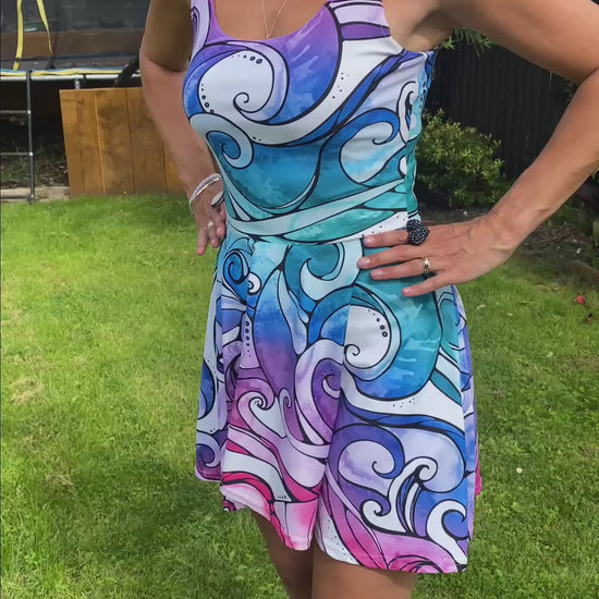 A woman wearing a bright rainbow wave flared dress, showing all angles. Designed by MooksGoo