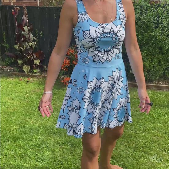 A lady wearing a blue and white illustrated sunflower flared skater dress in a garden, designed by MooksGoo