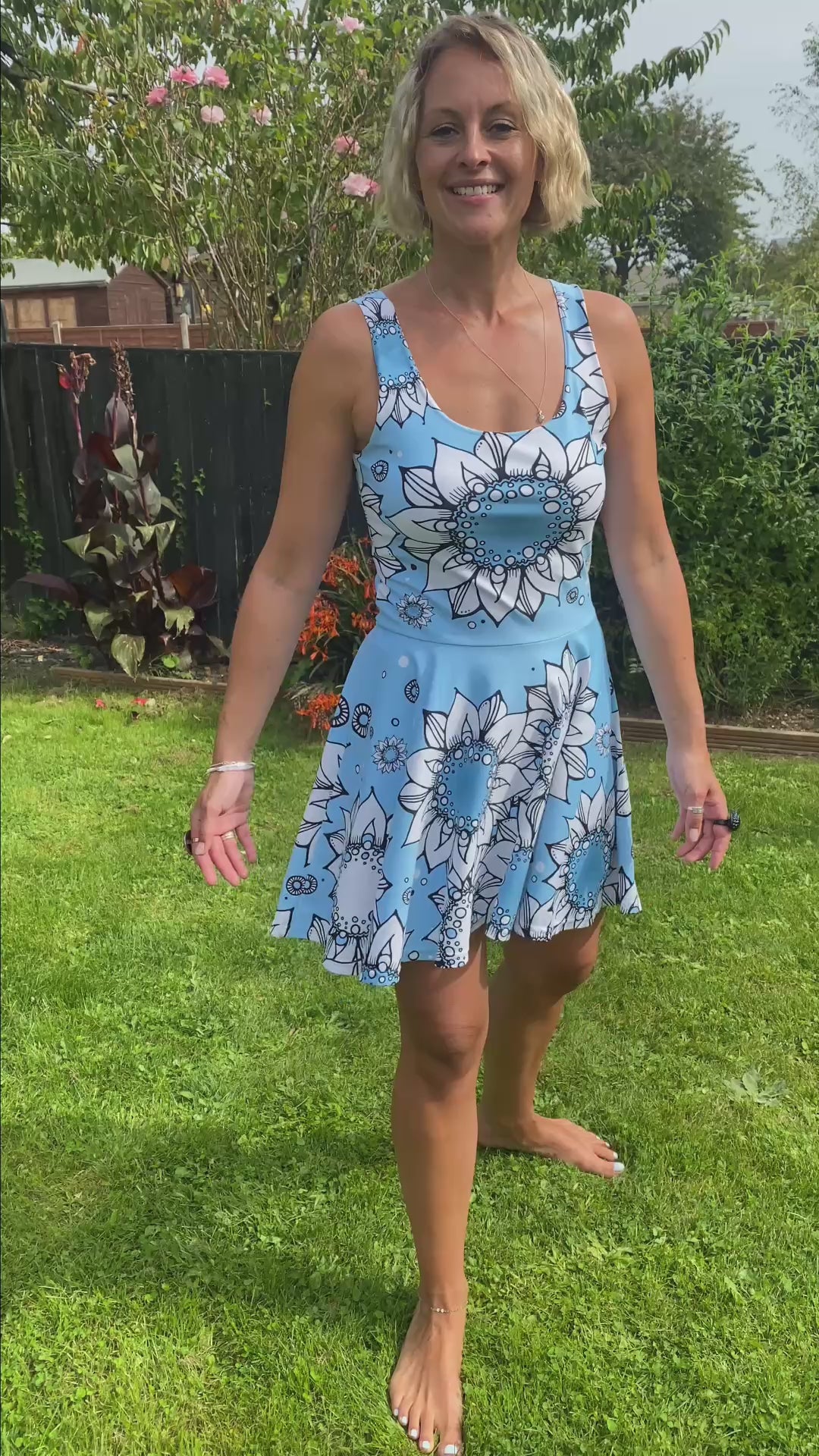 A lady wearing a blue and white illustrated sunflower flared skater dress in a garden, designed by MooksGoo