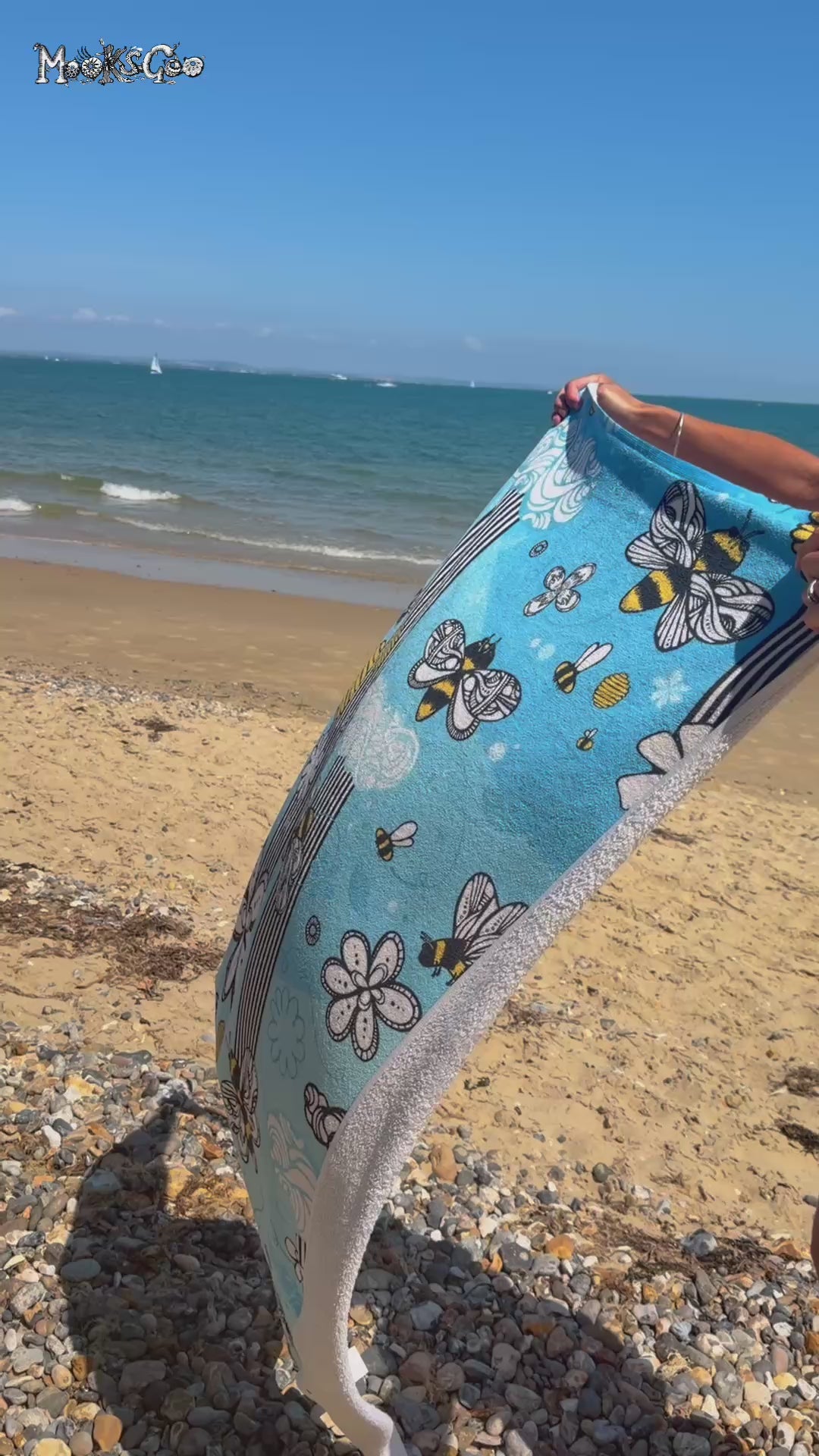 A lady holding a soft blue towel on the beach, with illustrated bees, honey, stripes and flowers, designed by MooksGoo