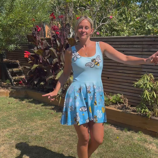 A young woman wearing a bright and bold bees, honey and flower illustrated sleeveless flared dress, designed by MooksGoo