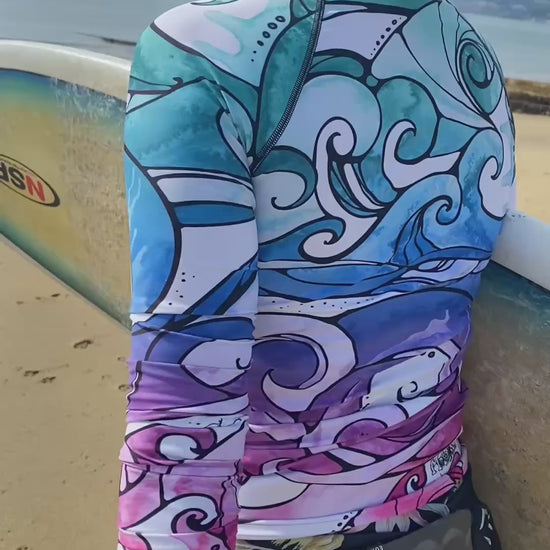 A lady with a surf board wearing a bright and colourful rainbow long sleeved rash guard with swirling waves, designed by MooksGoo