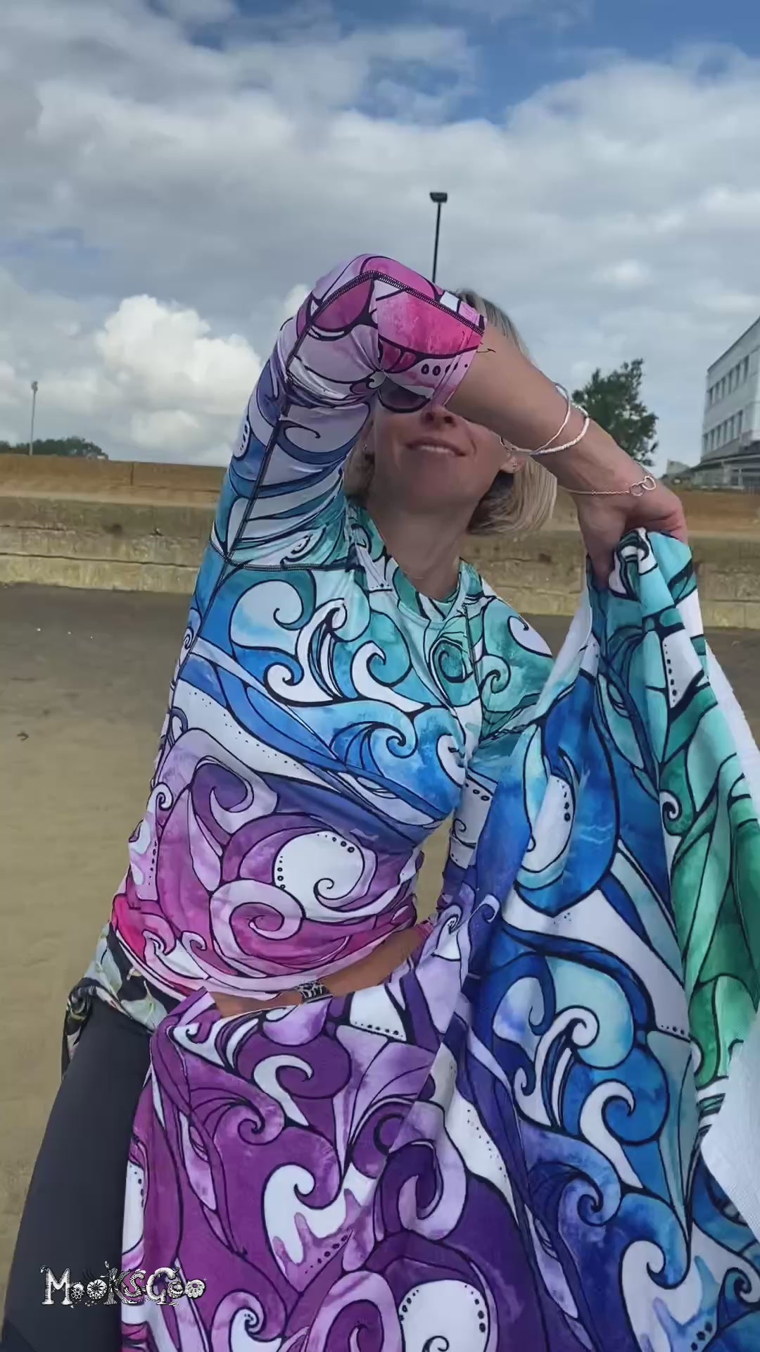 a woman wearing a rainbow wave rash vest is holding a bright funk colourful rainbow-coloured towel with illustrated waves, designed by MooksGoo
