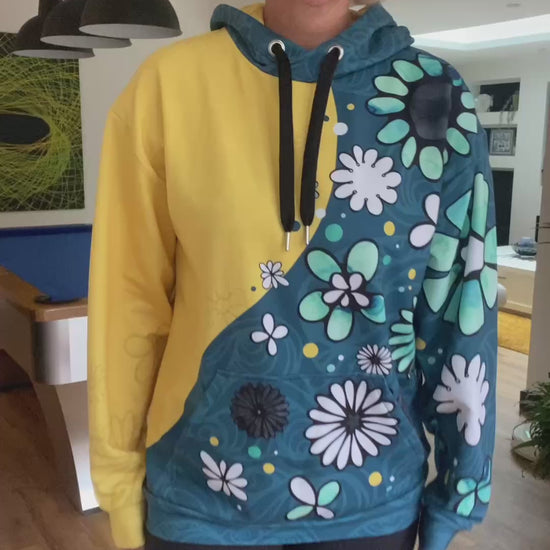 A lady wearing a split-coloured yellow and teal hoodie with illustrated flowers and dots, walking in a modern home with quirky interior, designed by MooksGoo
