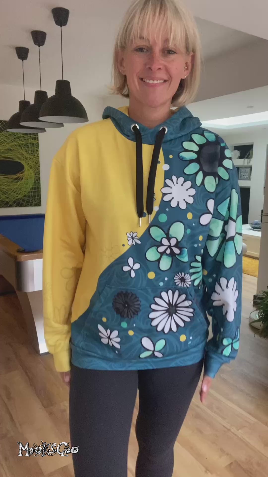 A lady wearing a split-coloured yellow and teal hoodie with illustrated flowers and dots, walking in a modern home with quirky interior, designed by MooksGoo